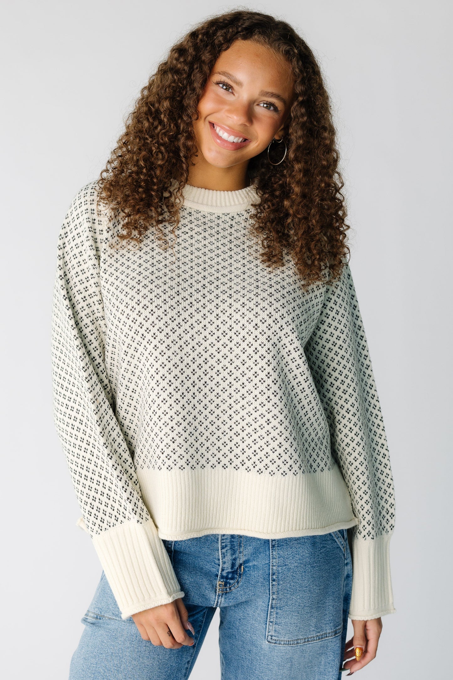 Teen girl wearing a loose fitting cream and black patterned pullover with wide ribbed cuffs and waist