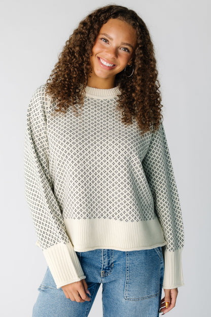 Teen girl wearing a loose fitting cream and black patterned pullover with wide ribbed cuffs and waist