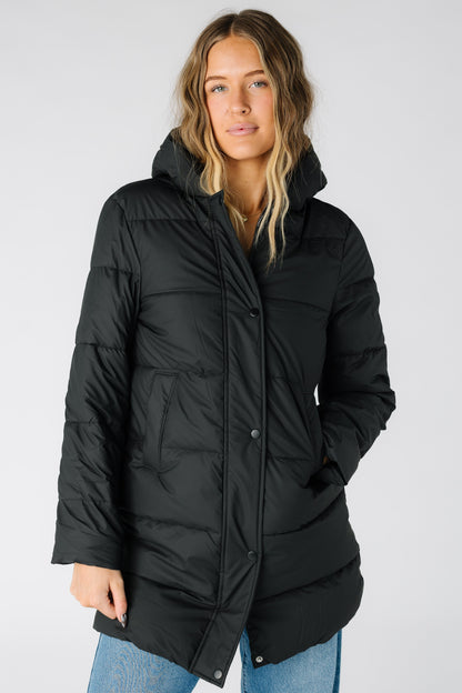 Woman wearing a a long sleeve black puffer jacket with pockets and a puffy hood