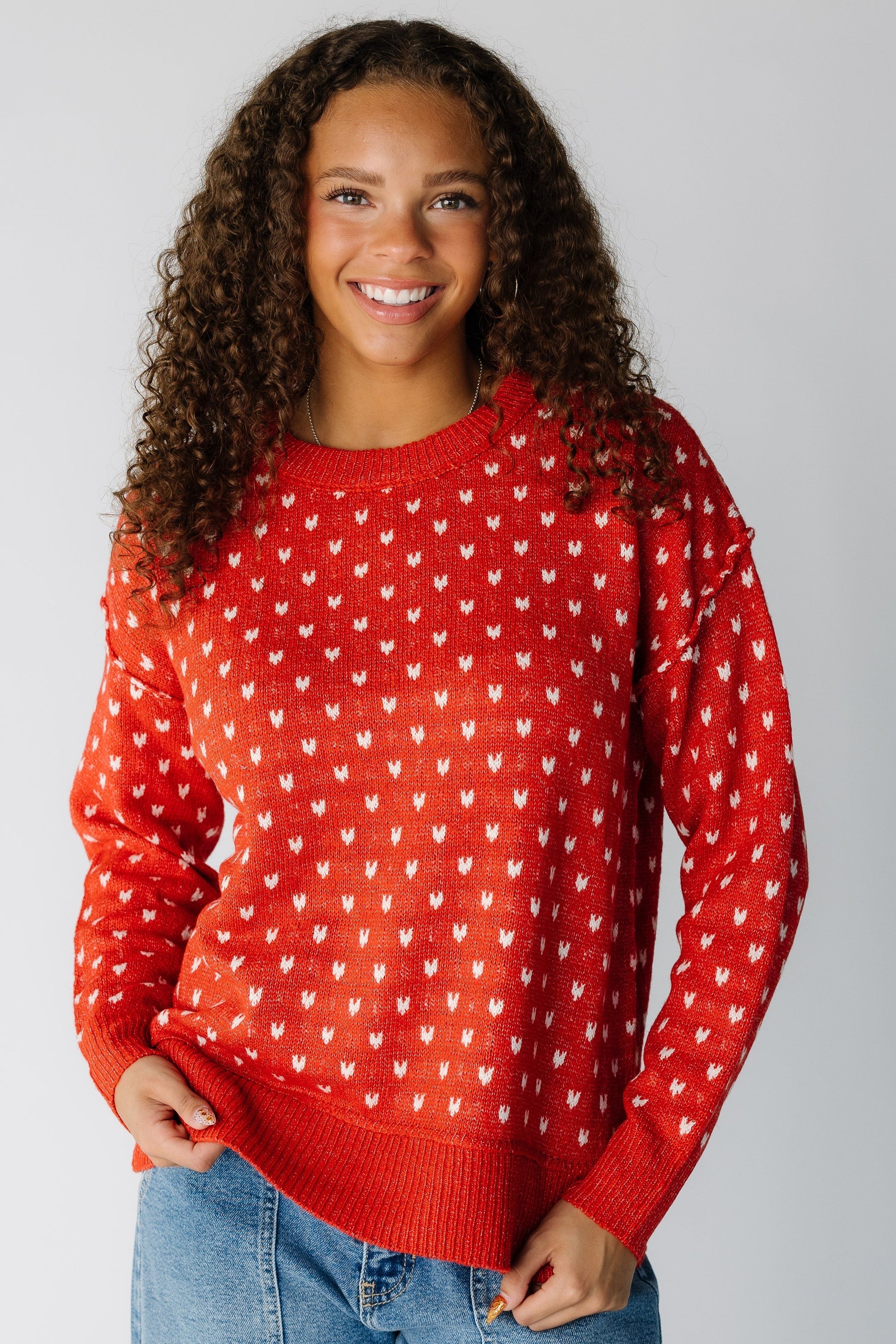 Woman wearing a modest long sleeve sweater with hearts, long sleeves and a crew neckline