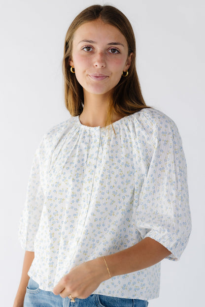 Woman wearing a white and blue floral print swing, button down top with a round neckline and elbow length sleeves.