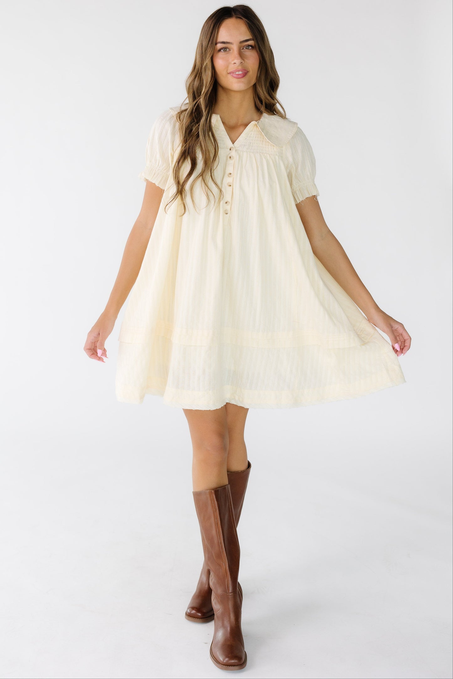 Woman wearing a cream textured stripe short dress with a V-neckline, rounded collar, and short puff sleeves.