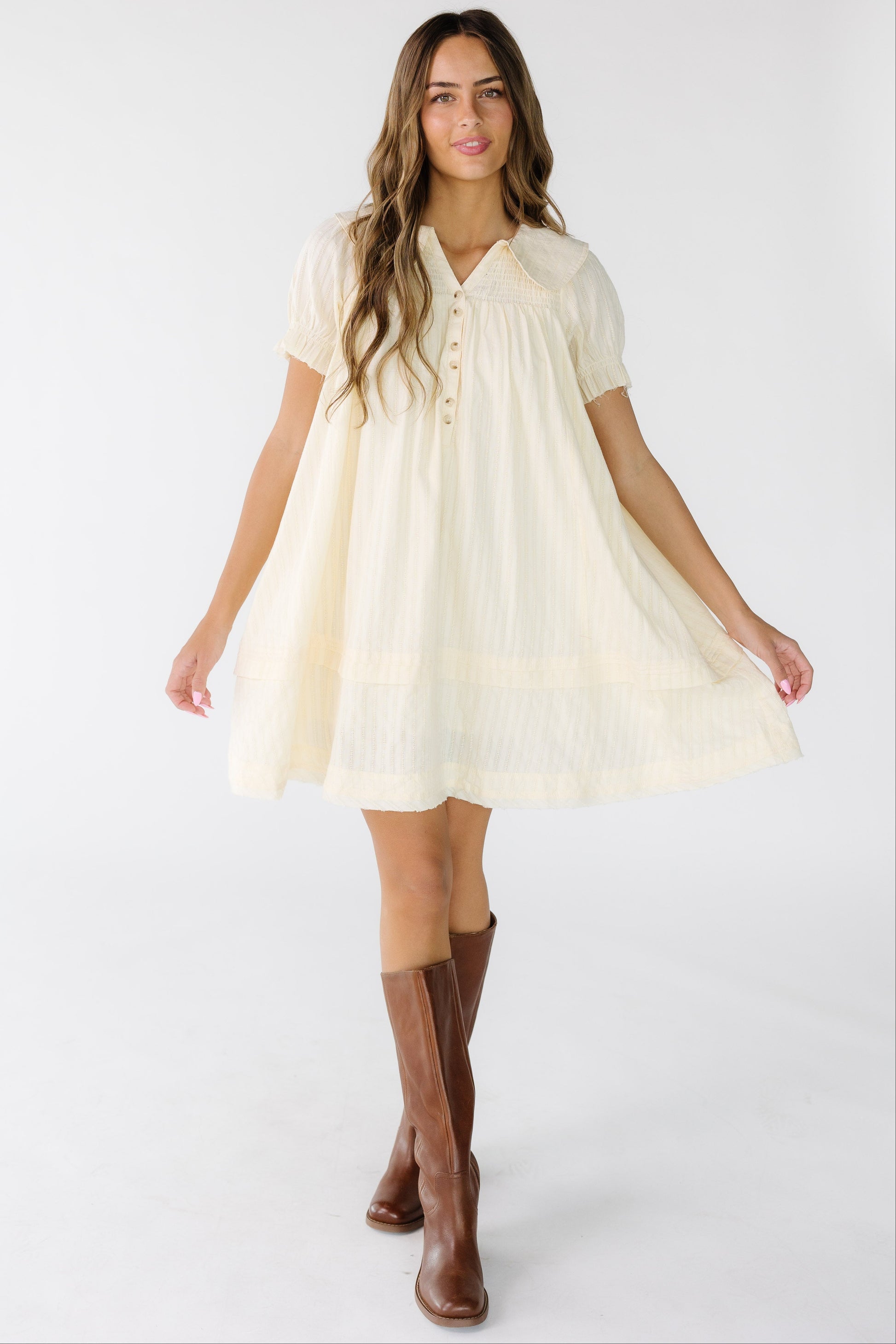 Woman wearing a cream textured stripe short dress with a V-neckline, rounded collar, and short puff sleeves.