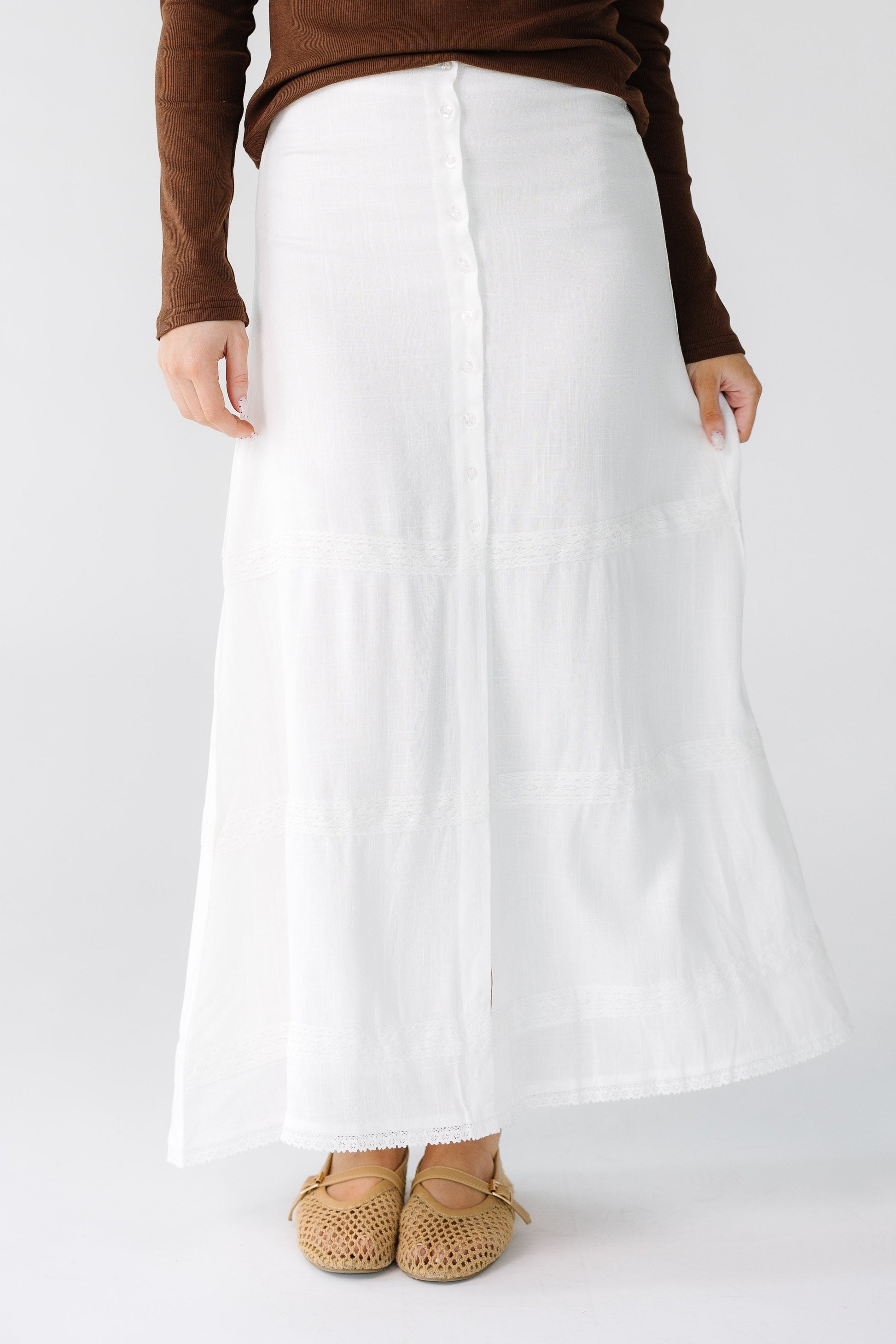 Woman wearing a  white button down midi skirt with 3 wide spread white lace stripes.