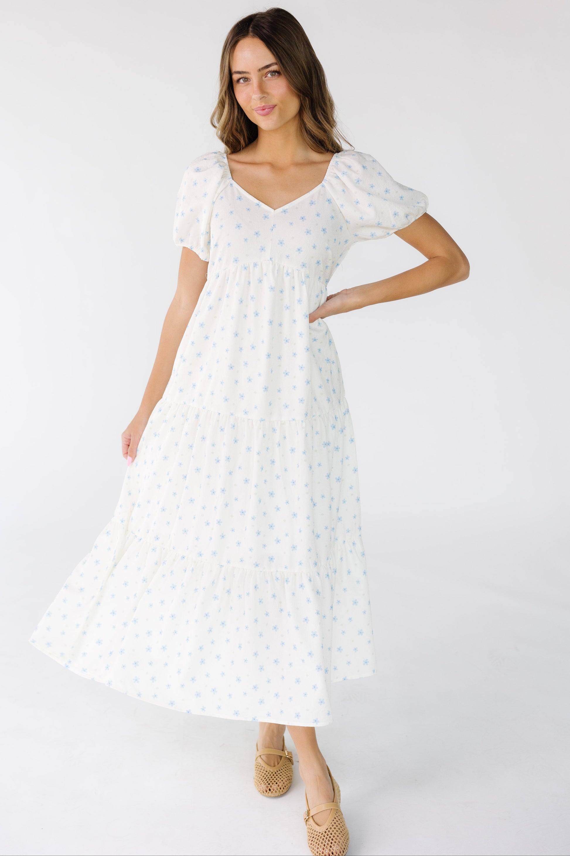 Young woman wearing a white midi-maxi dress with a full skirt with a close fitting bodice and large puff sleeves.