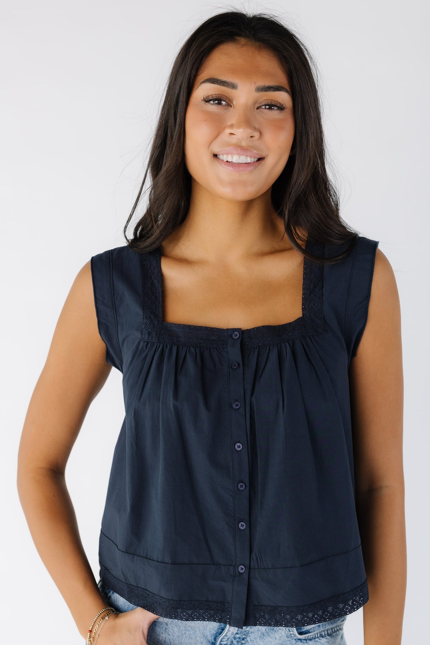 Woman wearing a loose fitting button down top with a square neckline and lace trim around the neckline and the hem.