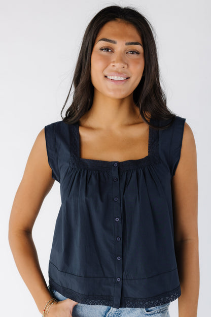 Woman wearing a loose fitting button down top with a square neckline and lace trim around the neckline and the hem.