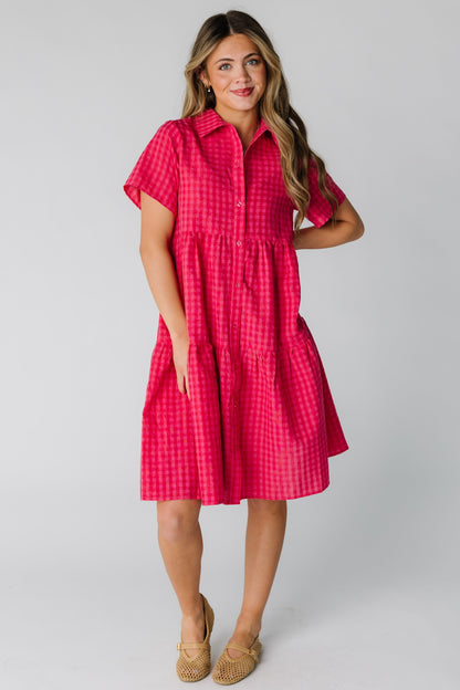 Woman wearing a loose fitting red and pink gingham dress with short sleeves and pointed collar.