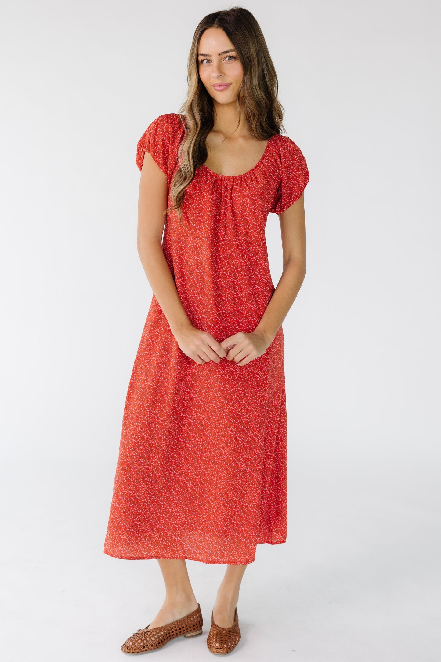 Woman wearing a red floral print midi dress that is loose fitting with a scoop neckline and short puff sleeves.