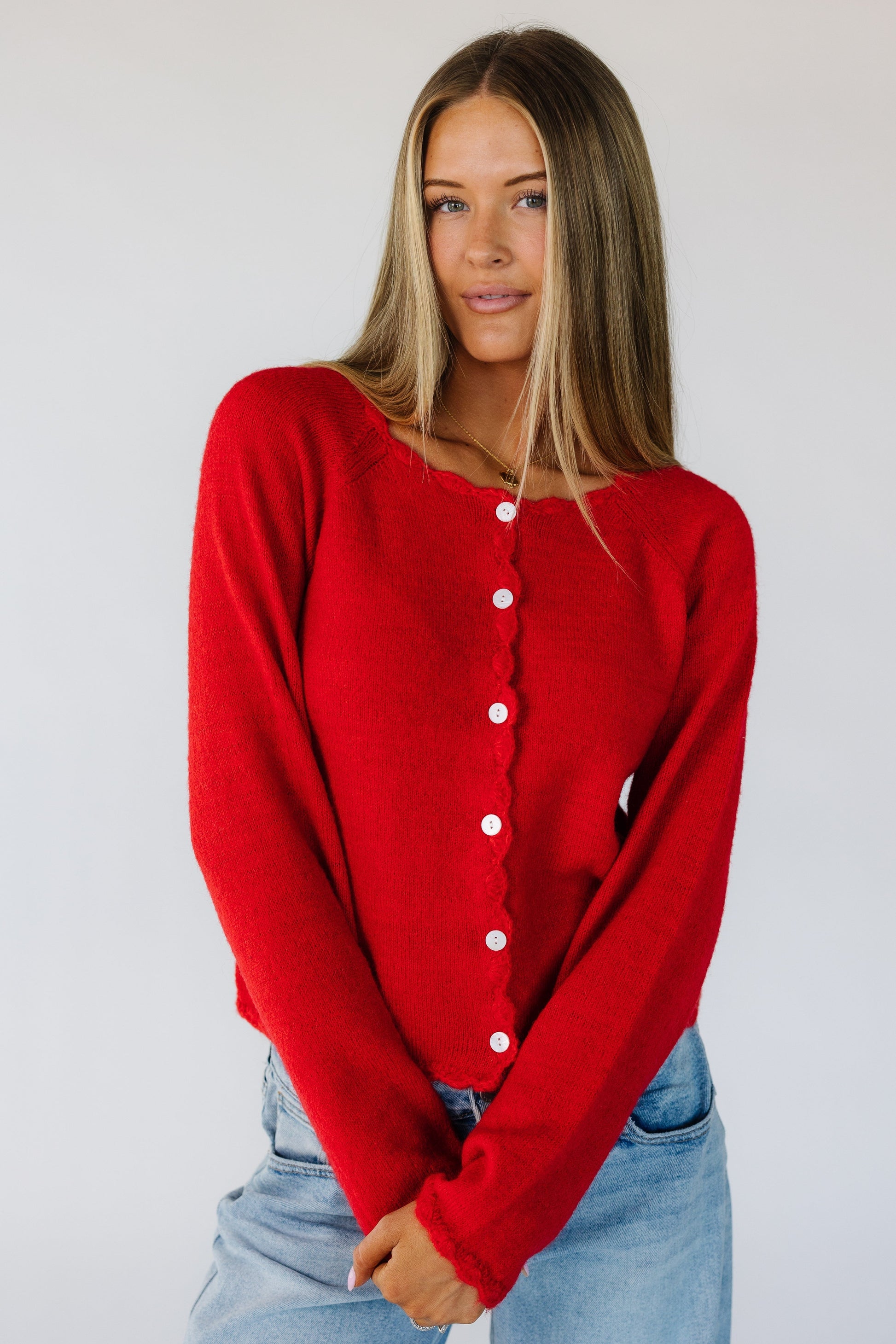 Woman wearing a modest red button down cardigan with a scallop edge round neckline and long sleeves with scallop cuffs.