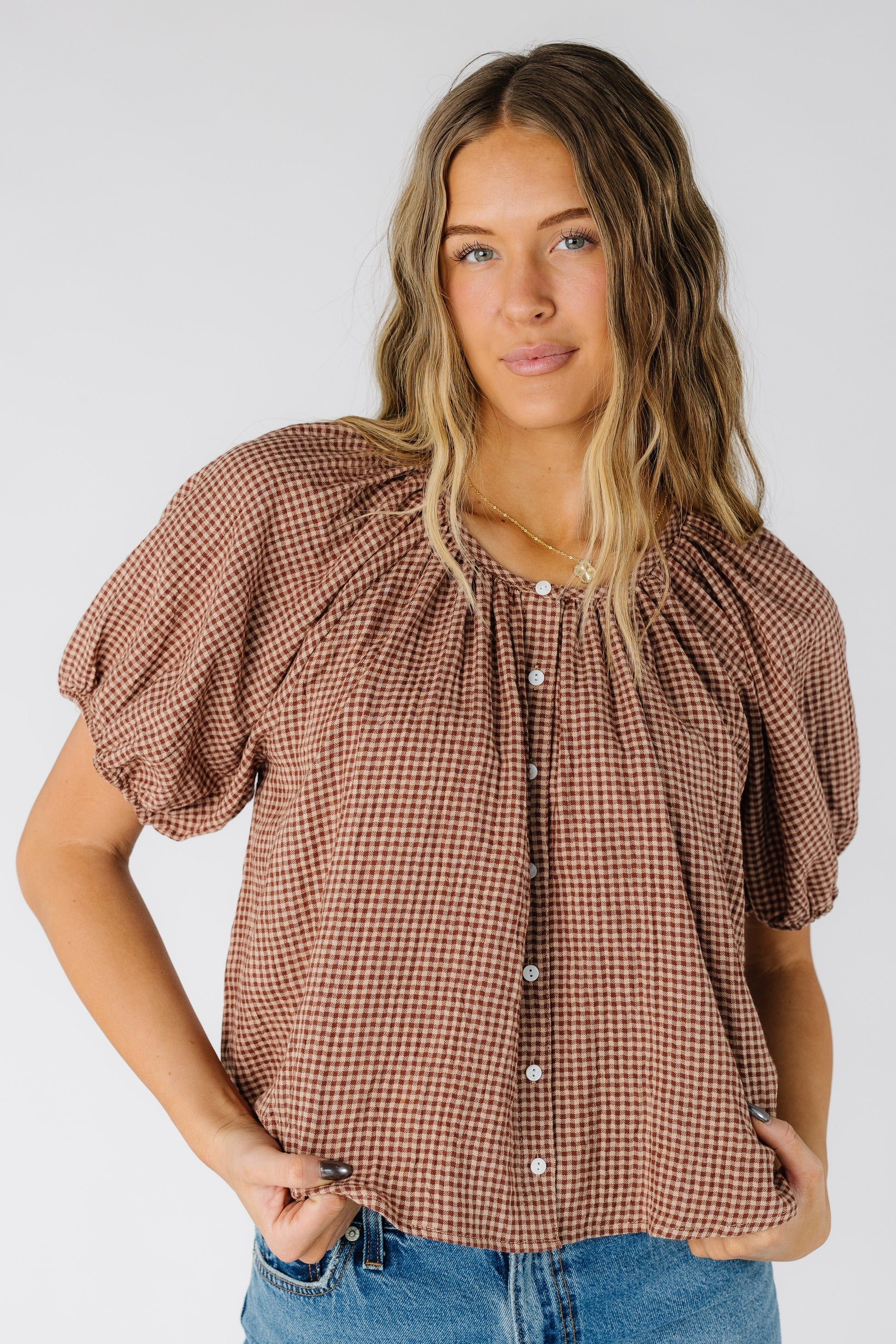 Woman wearing a modest taupe gingham button down top with scoop neckline and short puff sleeves