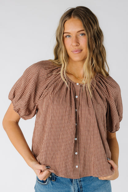 Woman wearing a modest taupe gingham button down top with scoop neckline and short puff sleeves