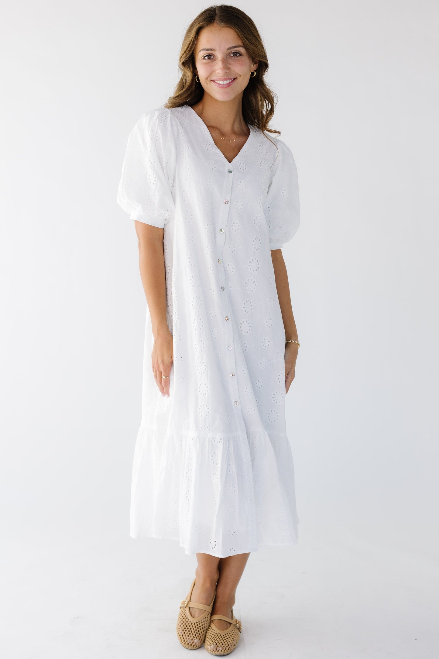 Woman wearing a white eyelet button down midi dress with a V-neckline, short sleeves and a wide bottom ruffle.