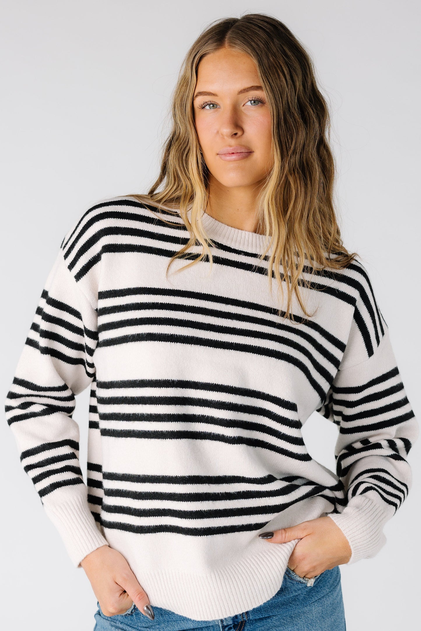 Woman wearing a modest long sleeve pullover sweater with a crew neckline in a light beige and black stripe top