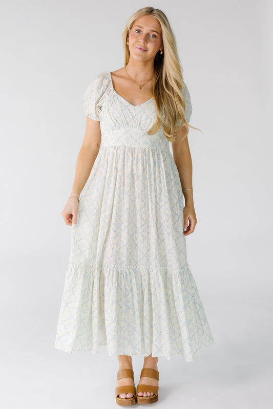 Woman wearing a white blue floral print midi dress wit a sweetheart neckline, short sleeves and a wide bottom ruffle.