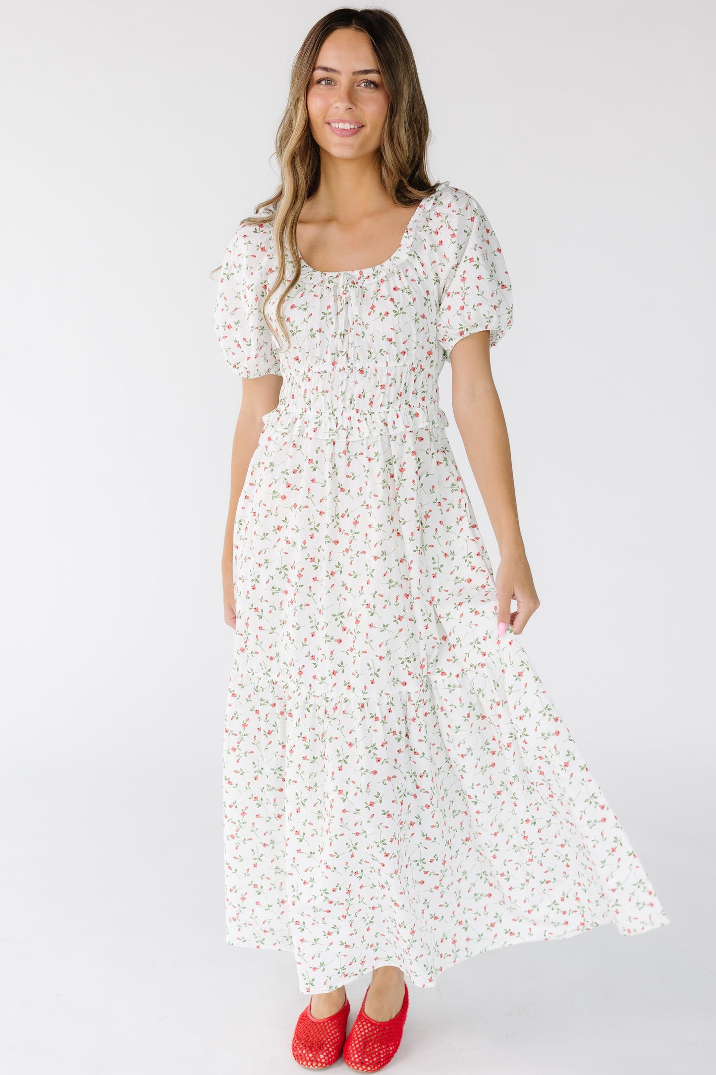 Woman wearing an ivory and red floral print midi-maxi dress with a scoop neckline, short sleeves and closer fitting bodice with a full skirt.