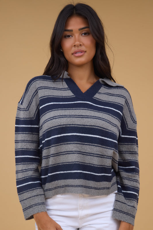 Young woman wearing a grey & navy stripe sweater with a V-neckline, pointed collar and long sleeves.