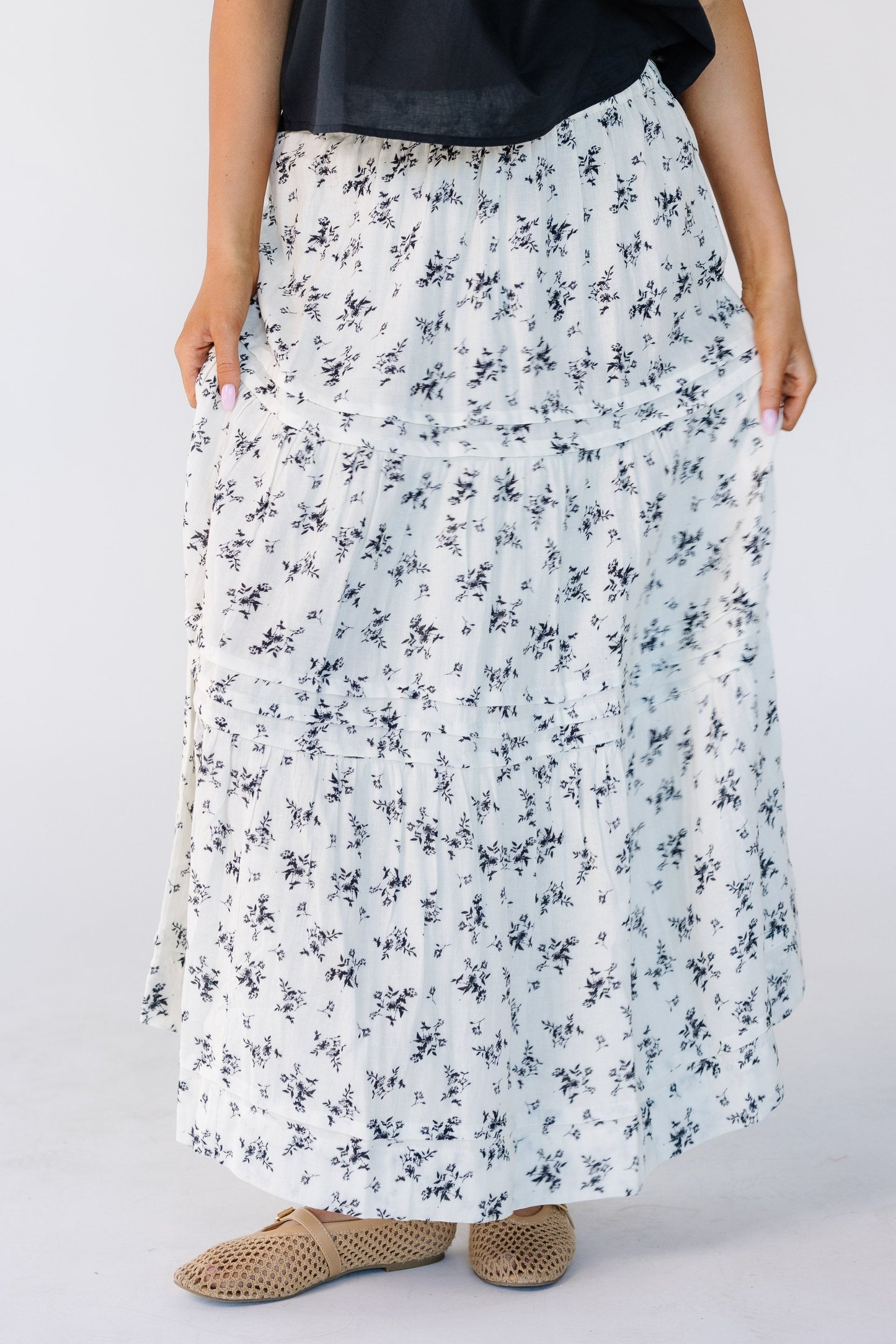 Woman wearing a modest white midi skirt with black floral print with horizontal tiers and pleats.