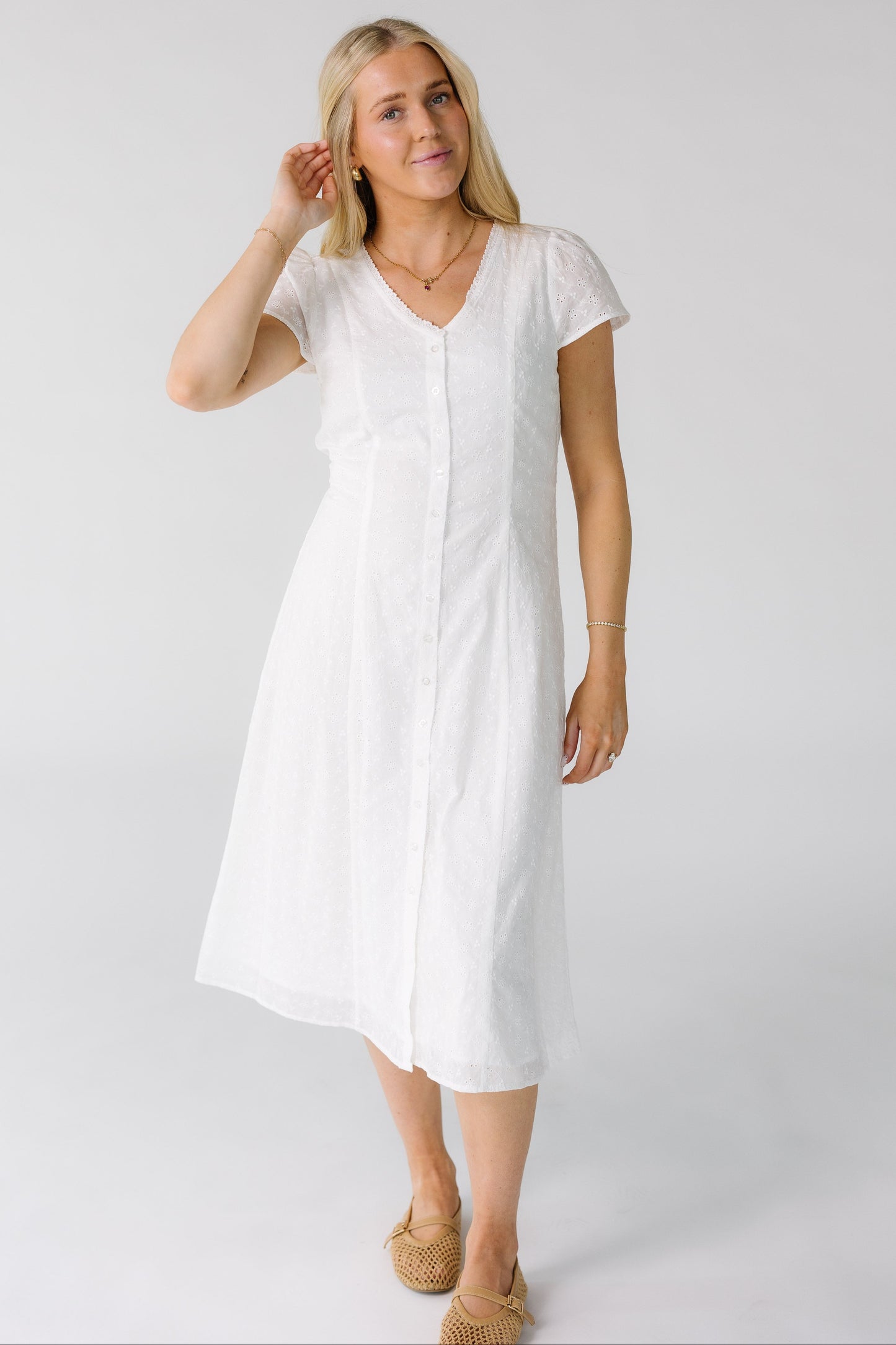 Woman wearing a white button down eyelet midi dress with a V-neckline and short sleeves.