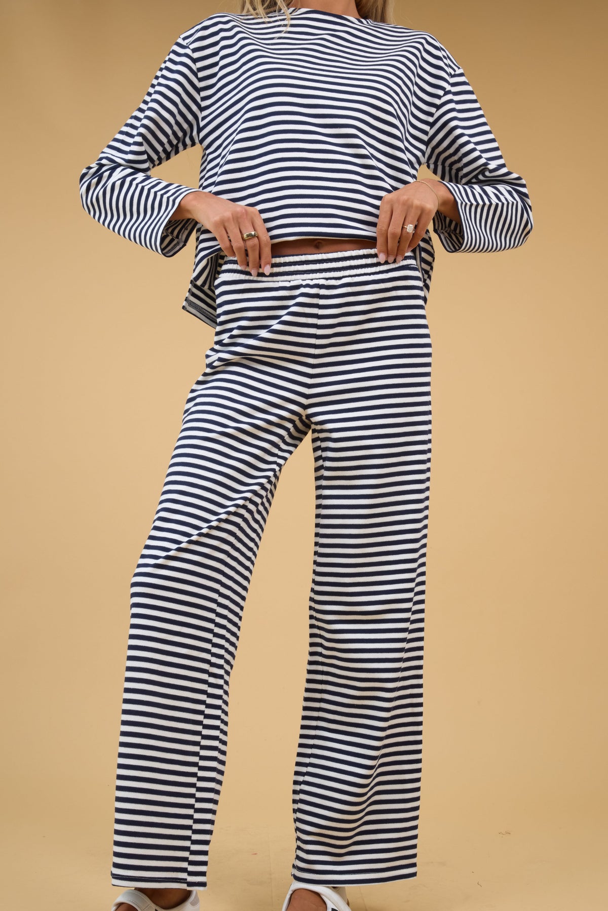 A woman wearing  a 2 piece lounge set in navy & white stripe with long sleeves and an elastic waistband.