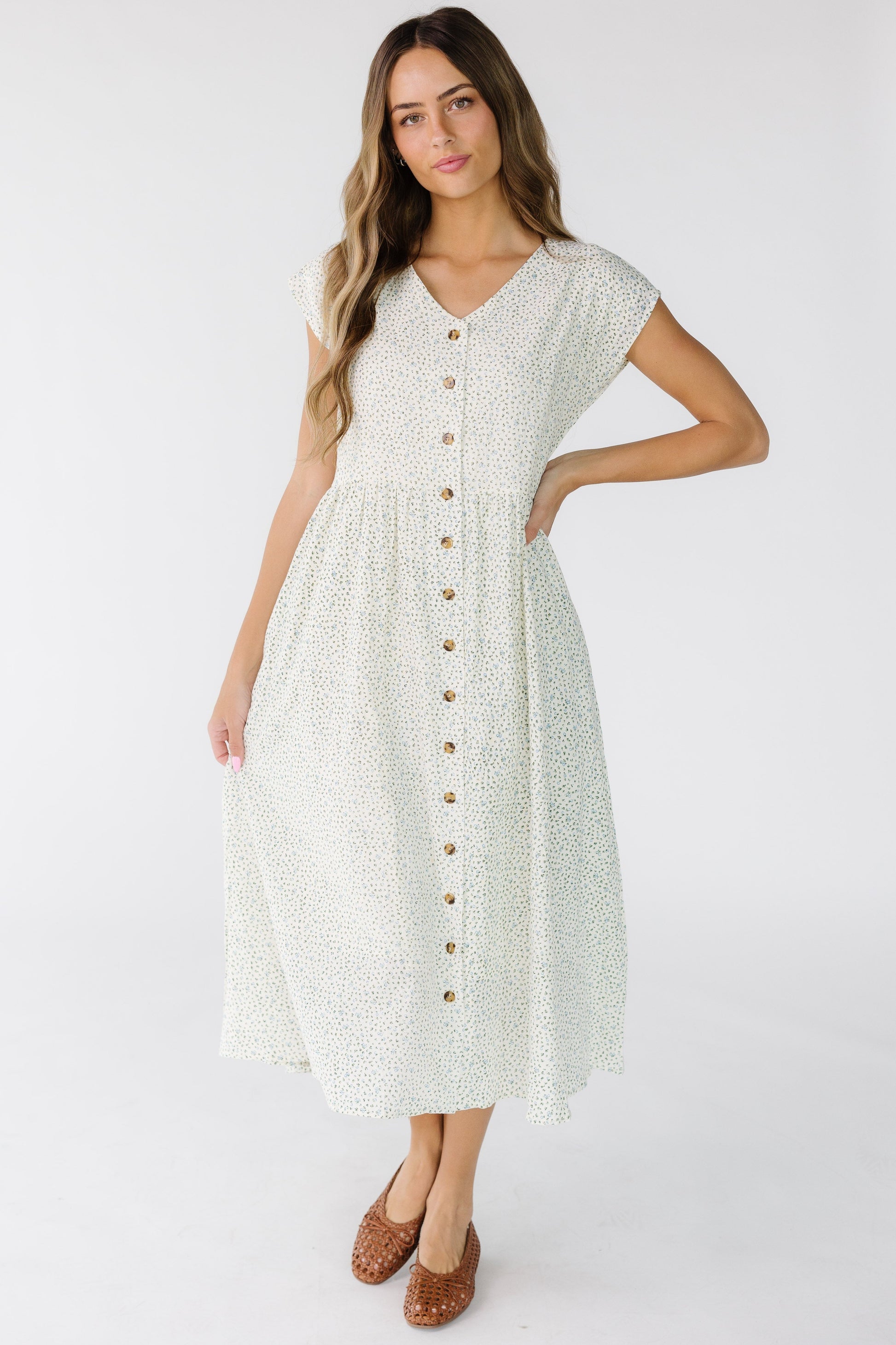 Woman wearing a modest loose fitting midi dress in white floral that buttons down the front with short sleeves and a V-neckline.