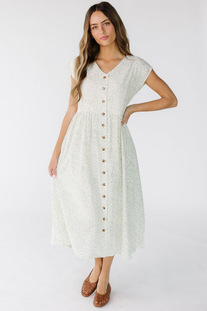 Woman wearing a modest loose fitting midi dress in white floral that buttons down the front with short sleeves and a V-neckline.