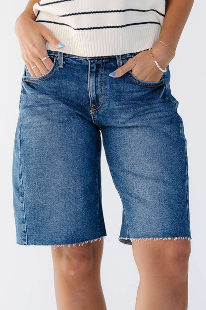 Close up view of a woman wearing a pair of modest dark denim shorts that are knee length.
