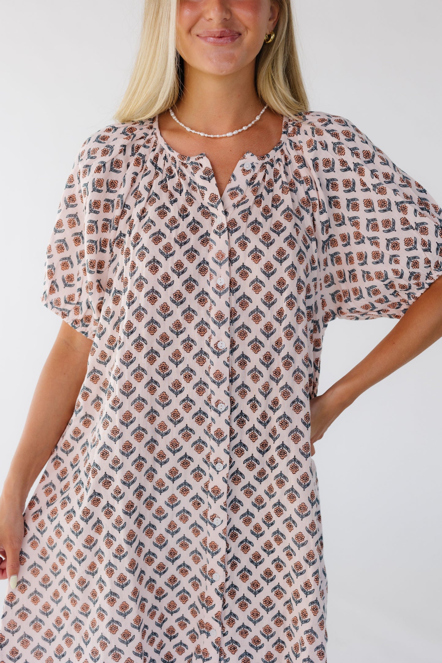 Closer view of a woman wearing a button down pink floral dress cut above the knee.