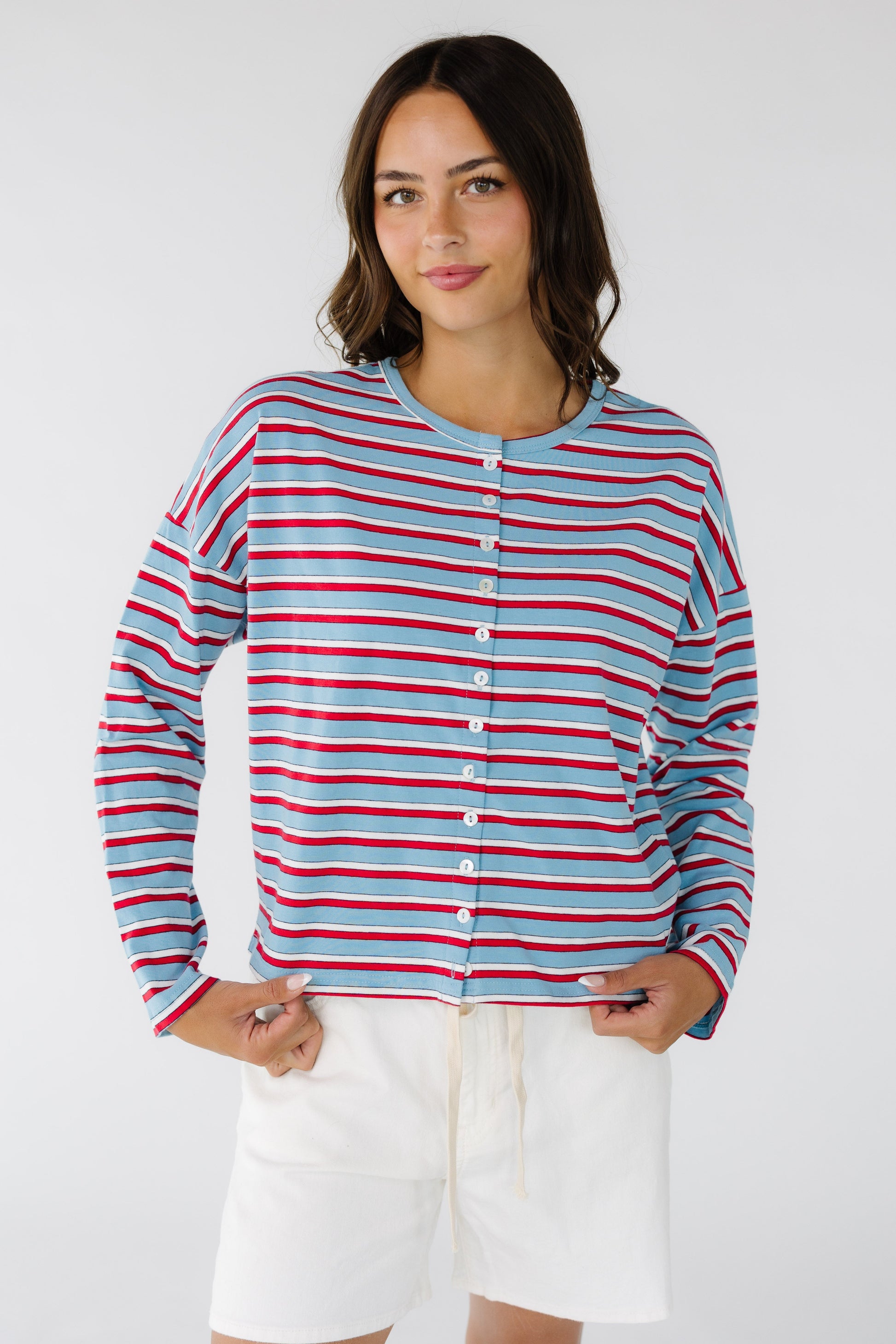 Woman wearing a boxy, long sleeve button down jersey cardigan in light blue, red & white stripe.