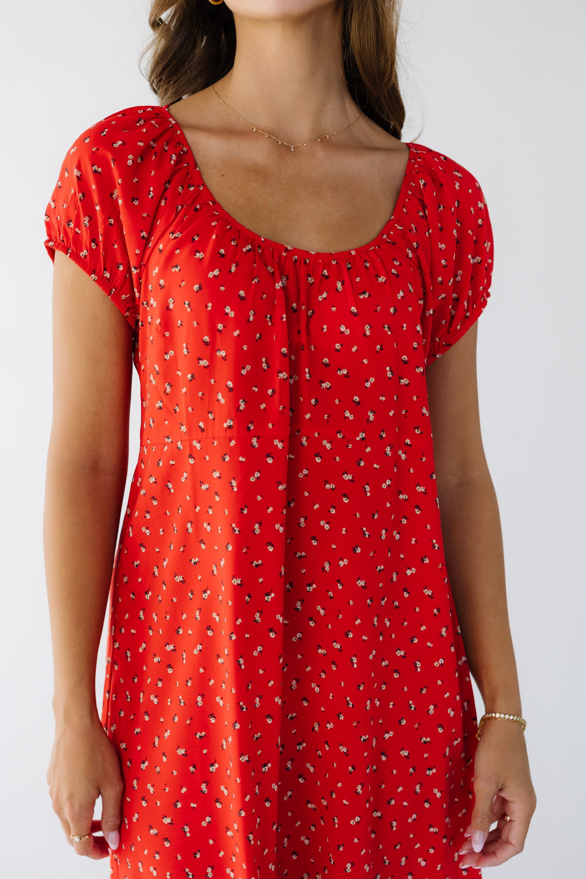 Closer view of a woman wearing a red floral loose fitting dress with a scoop neckline and short puff sleeves.