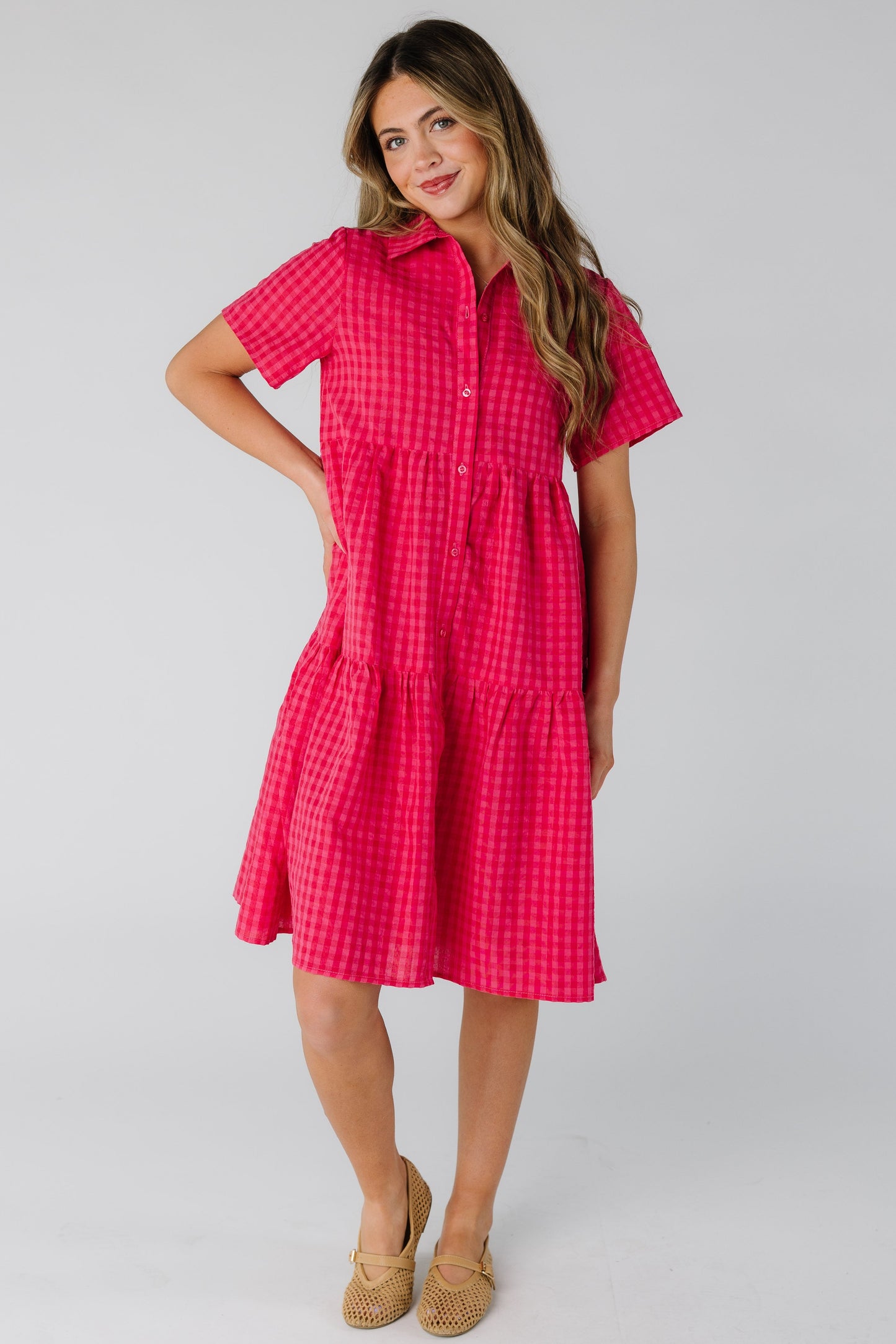 Woman wearing a red and pink gingham button down dress with short sleeves.