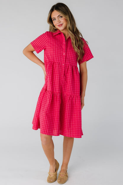 Woman wearing a red and pink gingham button down dress with short sleeves.