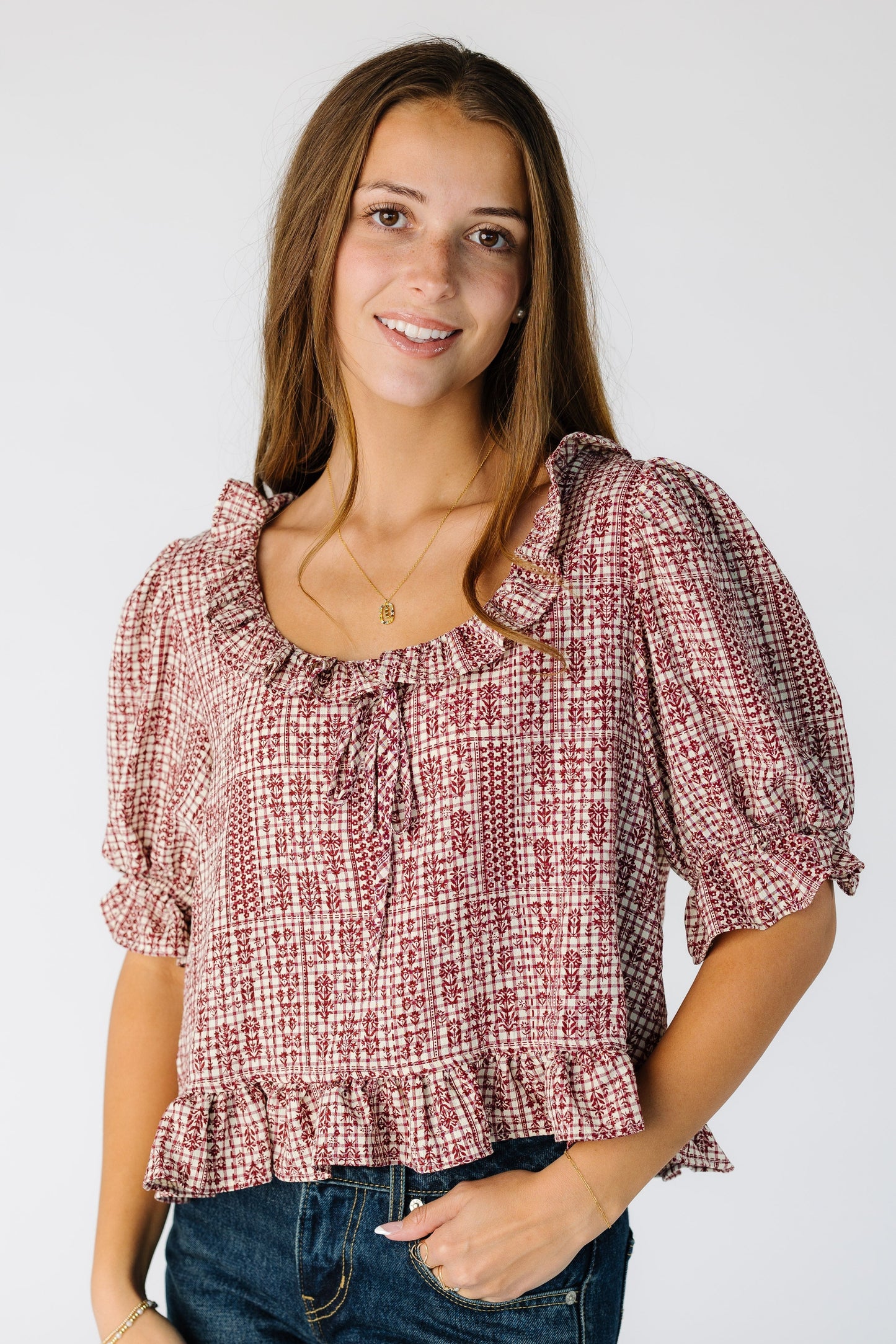 Woman wearing a red and white plaid blouse with a scoop neckline with ruffle and puff sleeves with a bottom ruffle