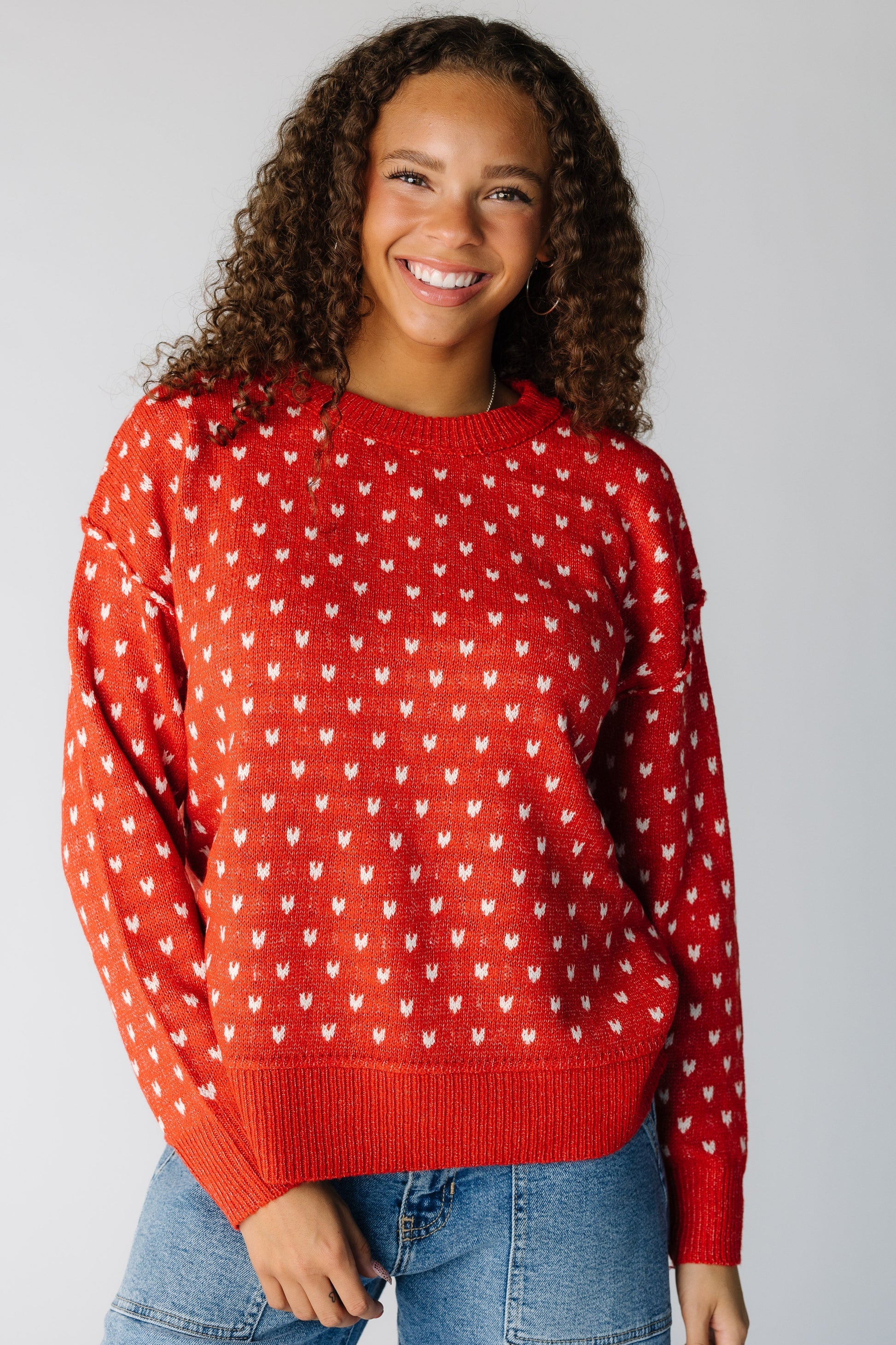 Woman wearing a red sweater with white hearts with long sleeves and exposed seams