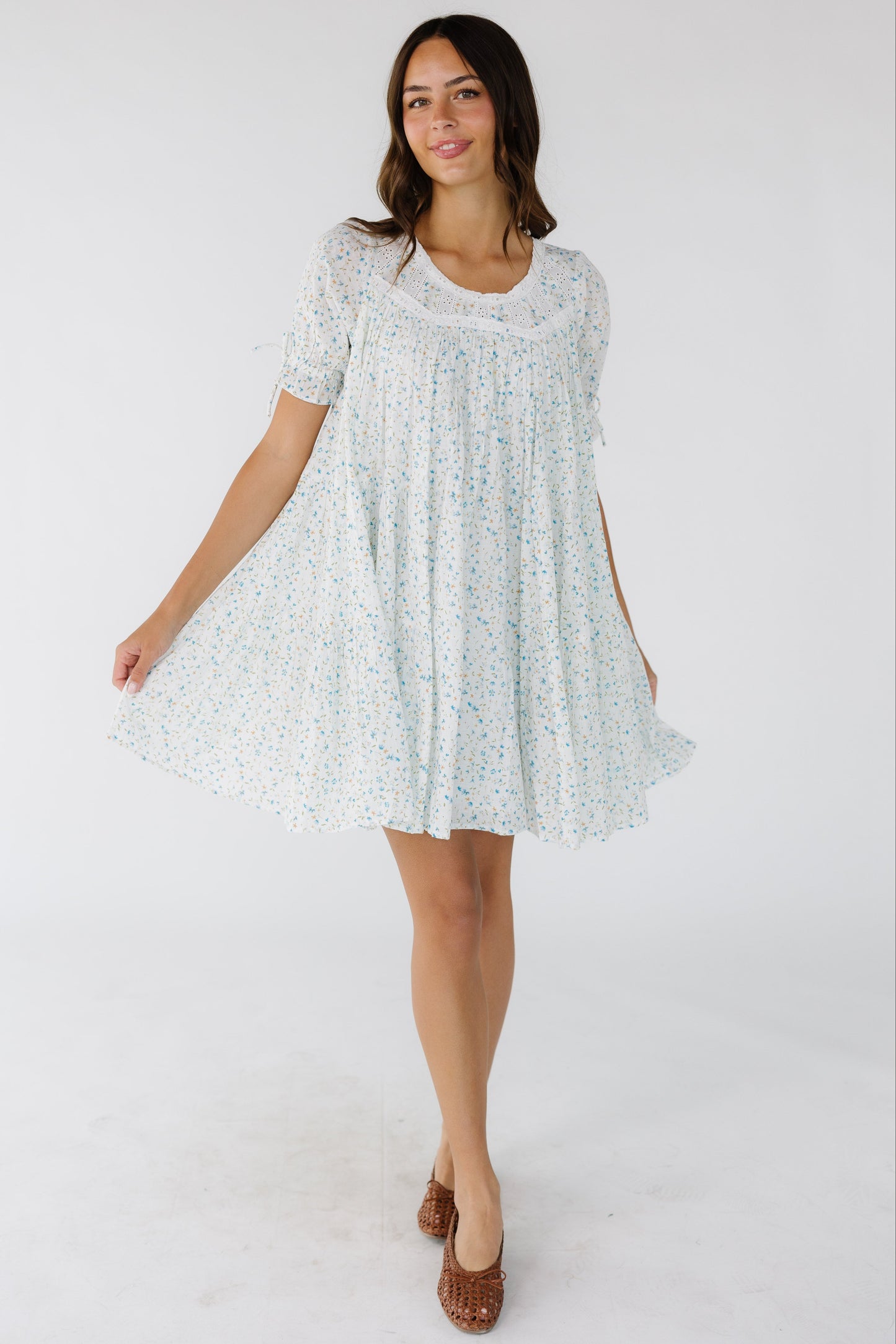 Woman woman wearing a white and blue floral print short dress with a round neckline and short puff sleeves.