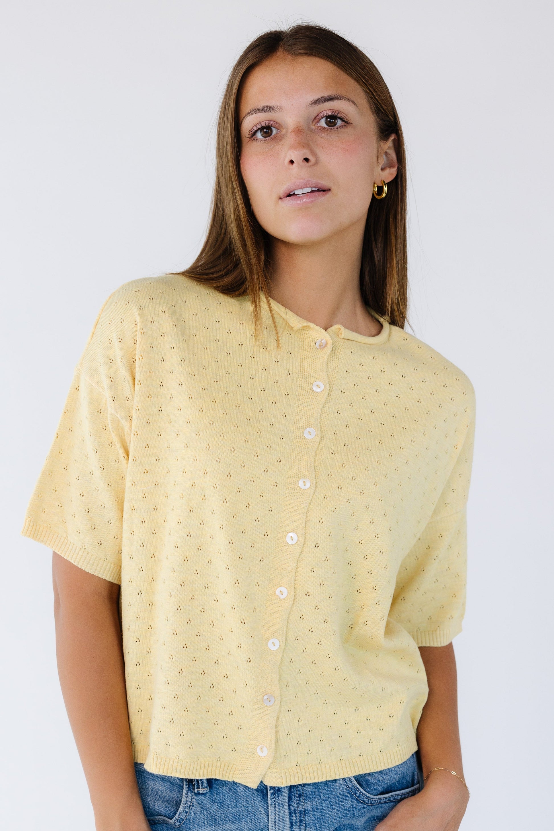 Young woman wearing a modest yellow button down cardigan in yellow pointelle eyelet knit with short sleeves.