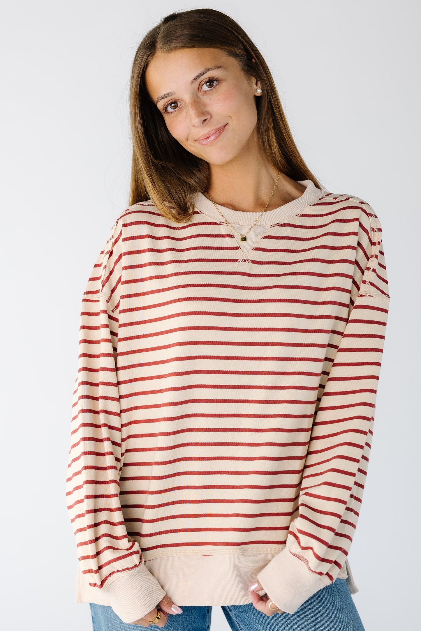 A woman wearing a loose fitting beige and brick stripe top