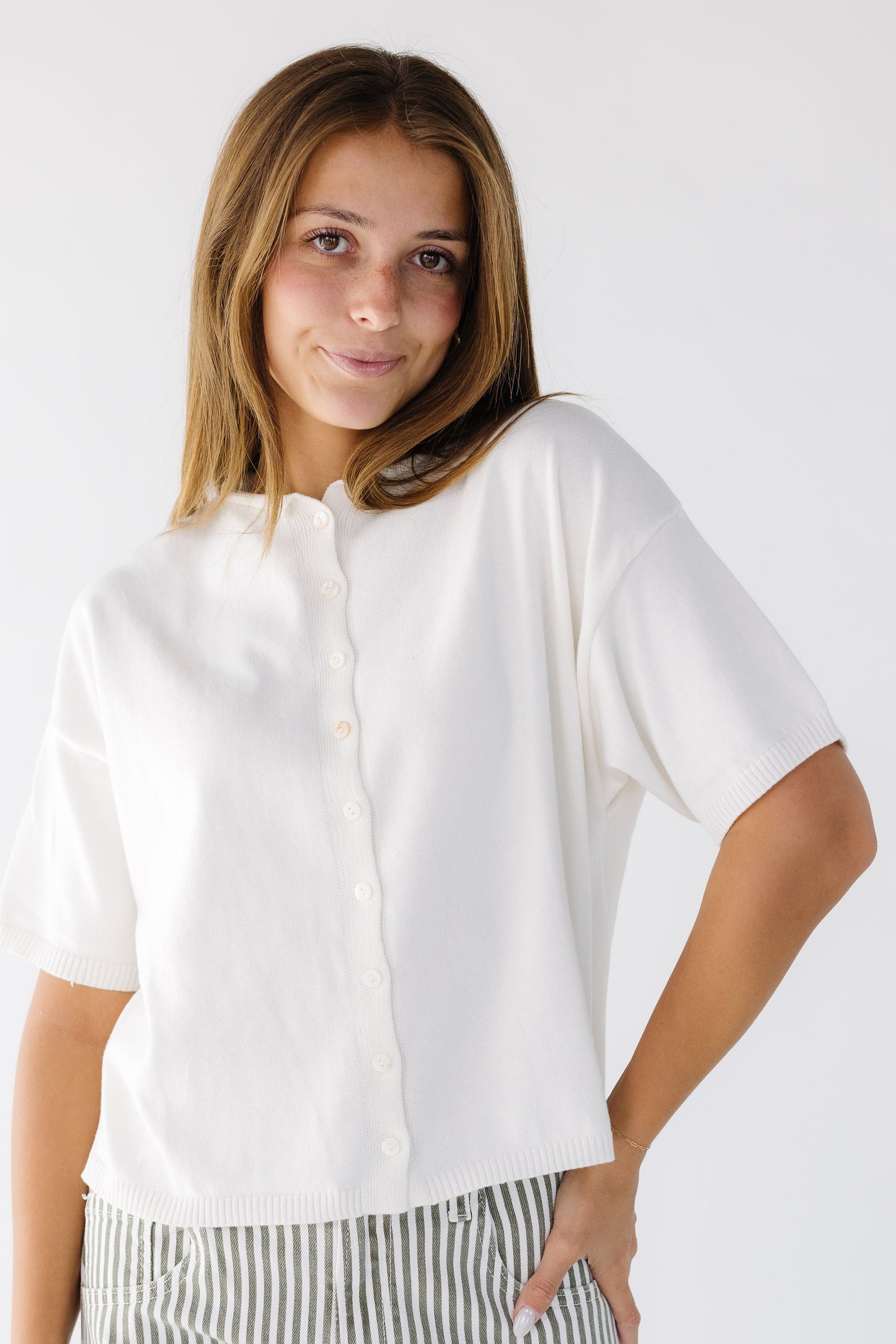 Young woman wearing an ivory loose fitting button down cardigan with short sleeves and a round neckline.