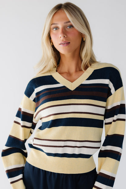 Woman wearing a yellow and multi-color stripe sweater with a V-neckline and long sleeves.
