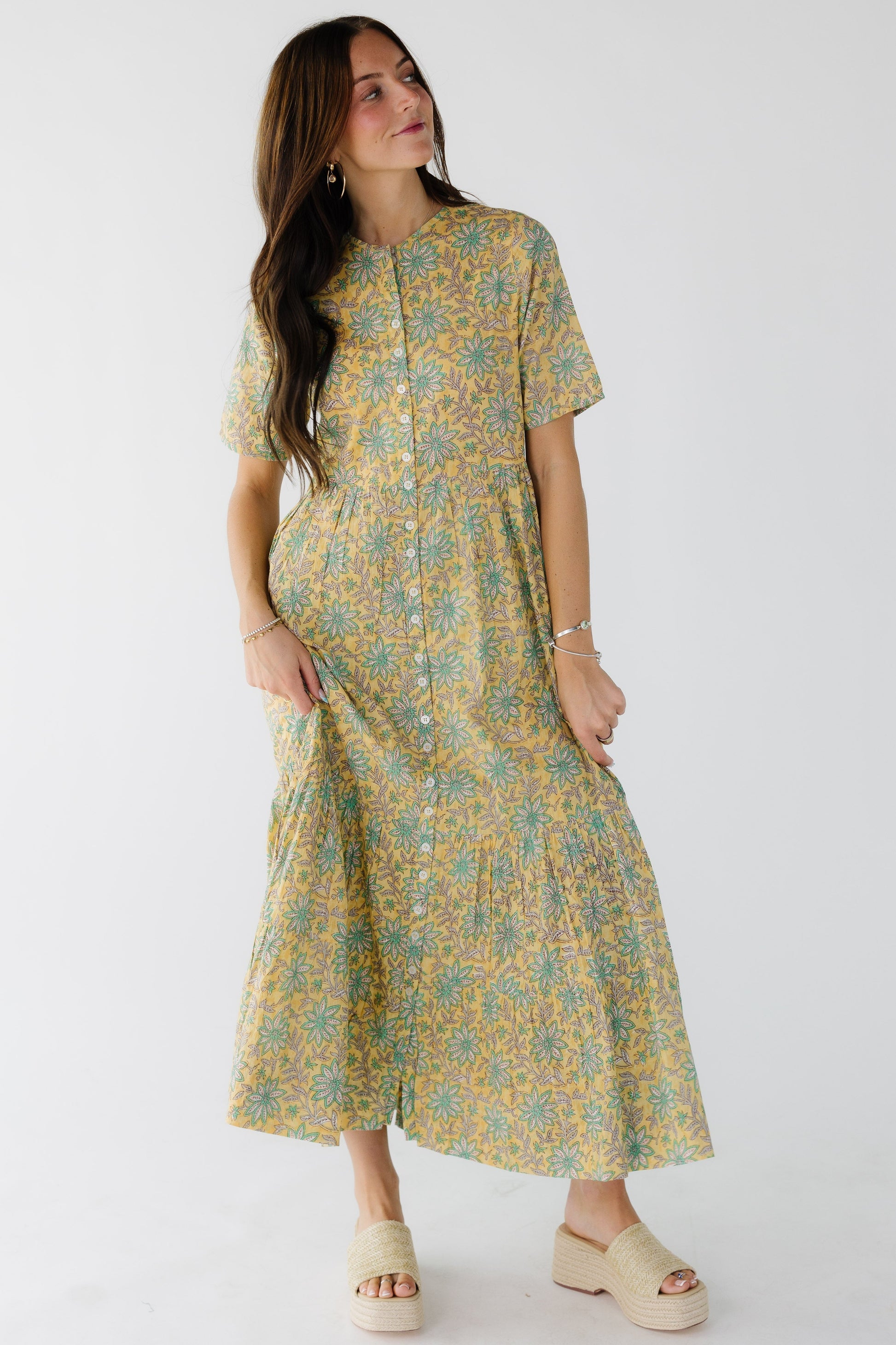 Woman wearing a yellow floral button down midi dress with shrot sleeves and a round neckline.