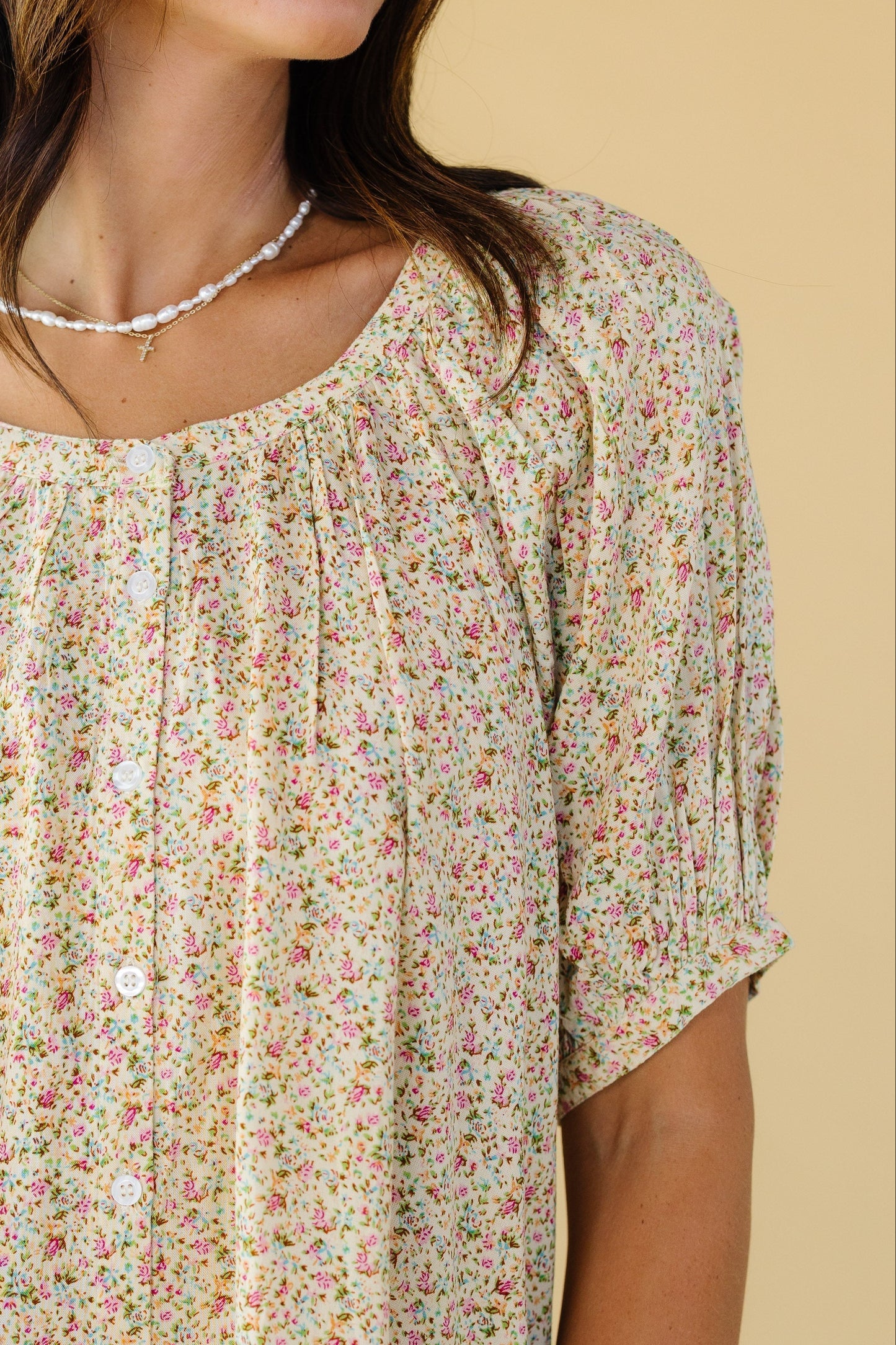 Close view of a woman wearing a yellow floral button down top with a round neckline and puff sleeves.