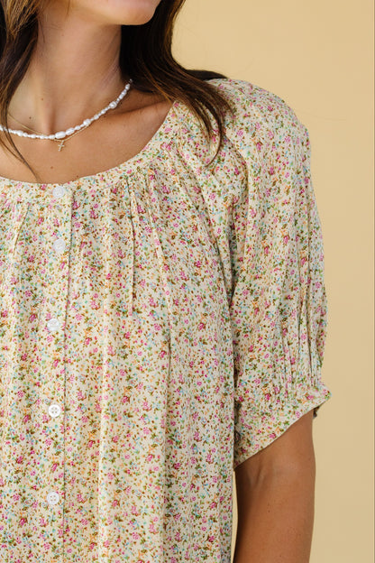 Close view of a woman wearing a yellow floral button down top with a round neckline and puff sleeves.