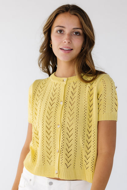 Young woman wearing a modest, lacey knit, button down cardigan with short sleeves and a crew neckline.
