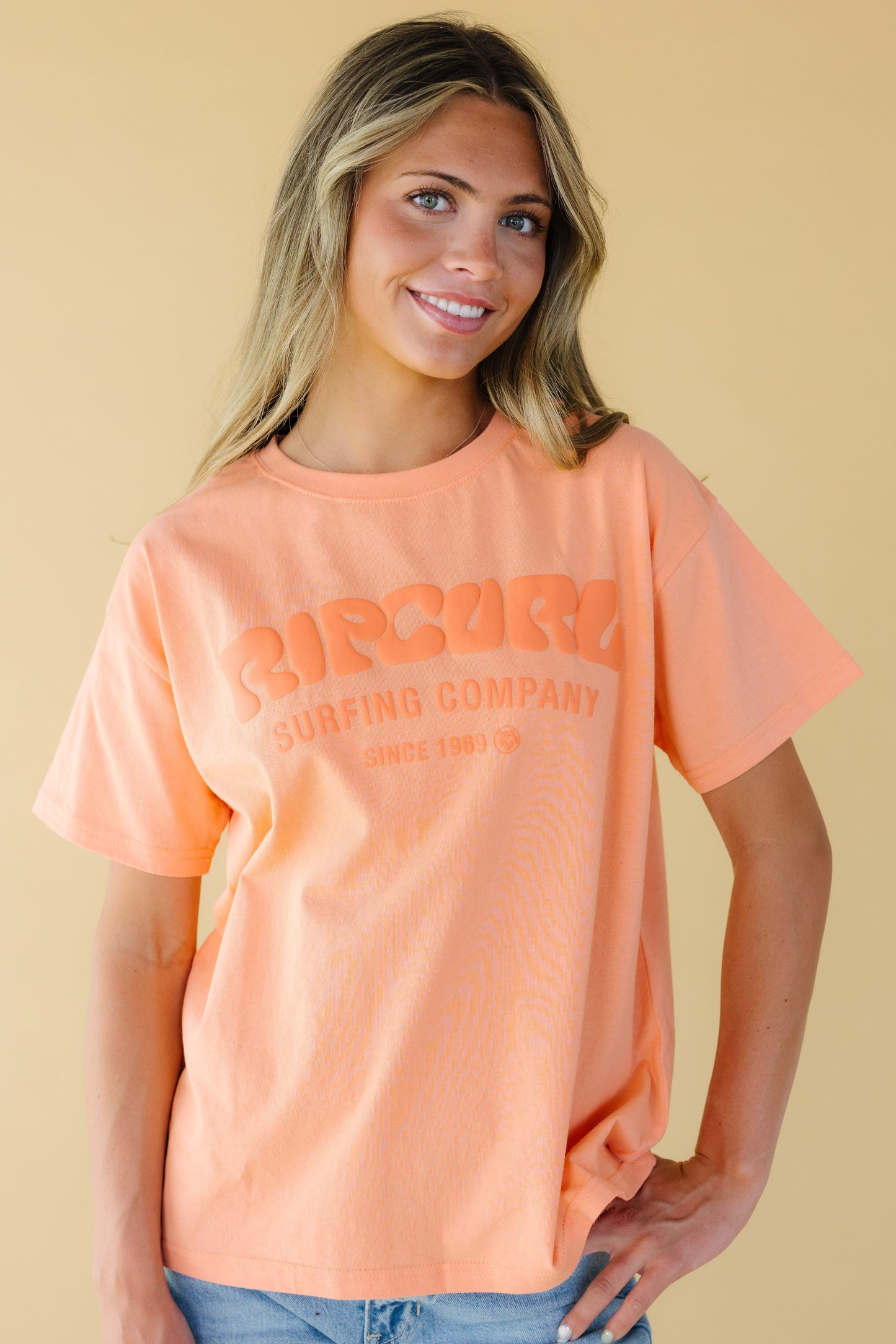 Young woman wearing a modest graphic tee in orange with short sleeves from Rip Curl.