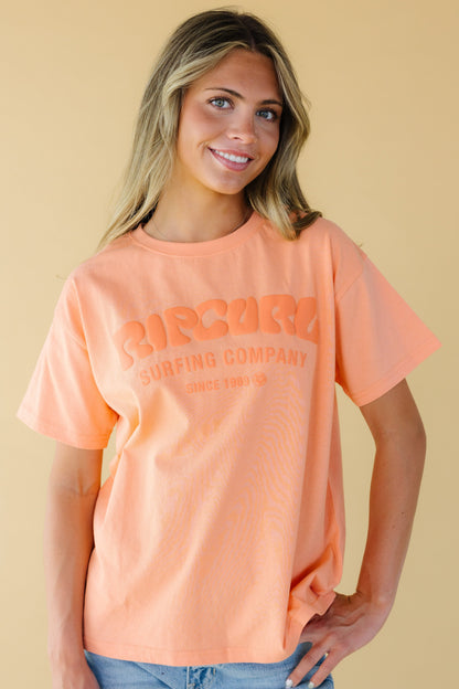 Young woman wearing a modest graphic tee in orange with short sleeves from Rip Curl.