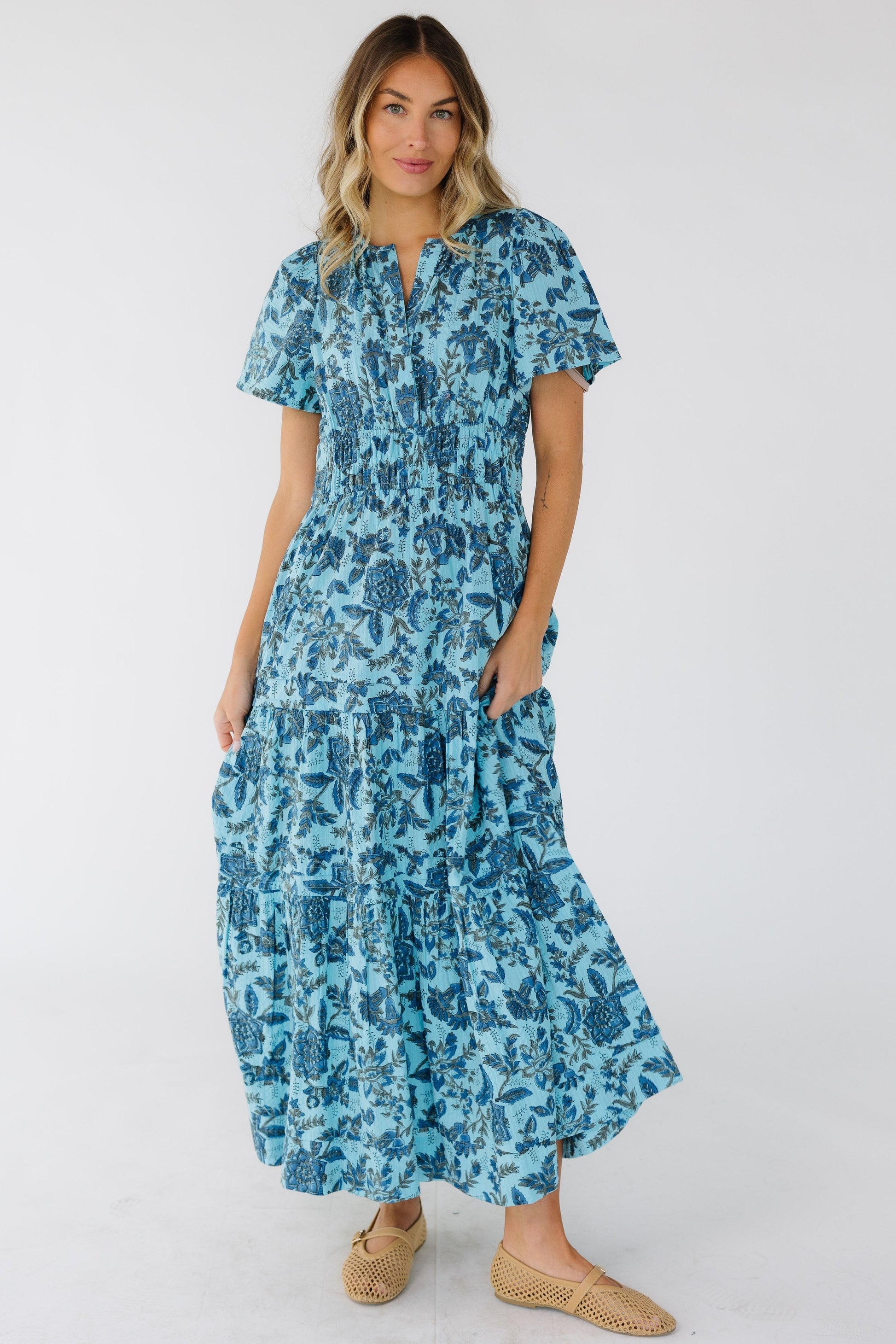 Woman wearing a blue print midi-maxi dress with a tiered and gathered skirt and short sleeves.
