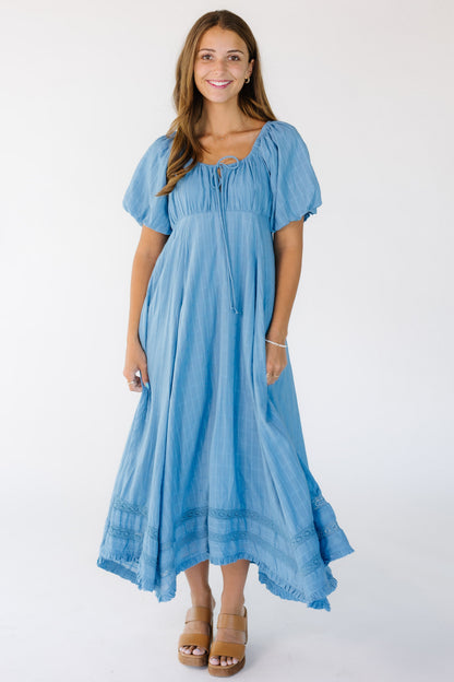 Young woman wearing a loose fitting, flowy midi-maxi dress in blue with an empire waist and balloon sleeves.