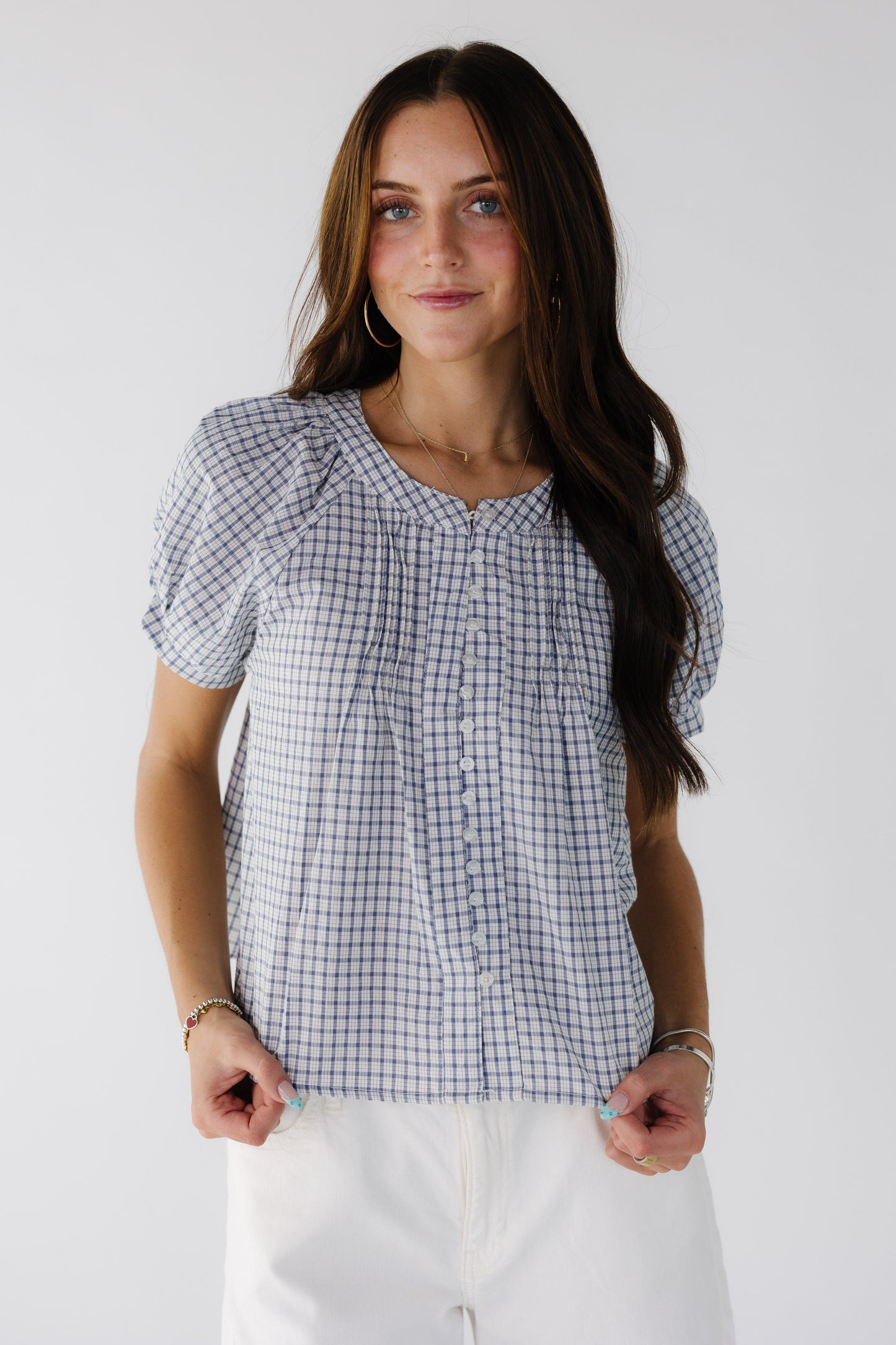 Woman wearing a blue & white plaid blouse with short puff sleeves and a round neckline.