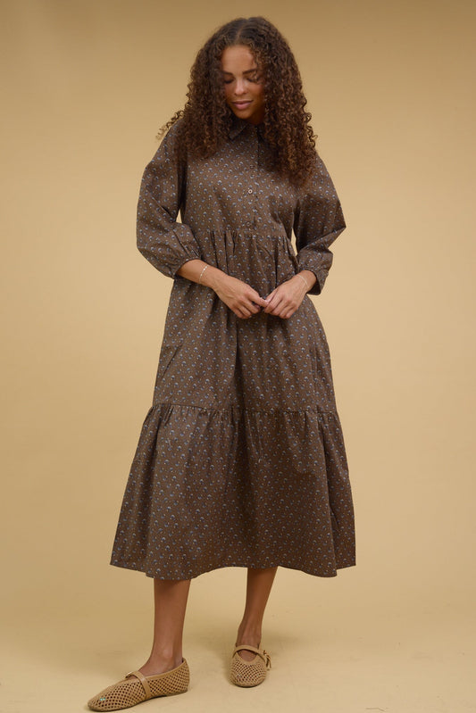 Young woman wearing a modest brown print midi dress with a button down bodice, long sleeves and a full gathered skirt and pointed collar.