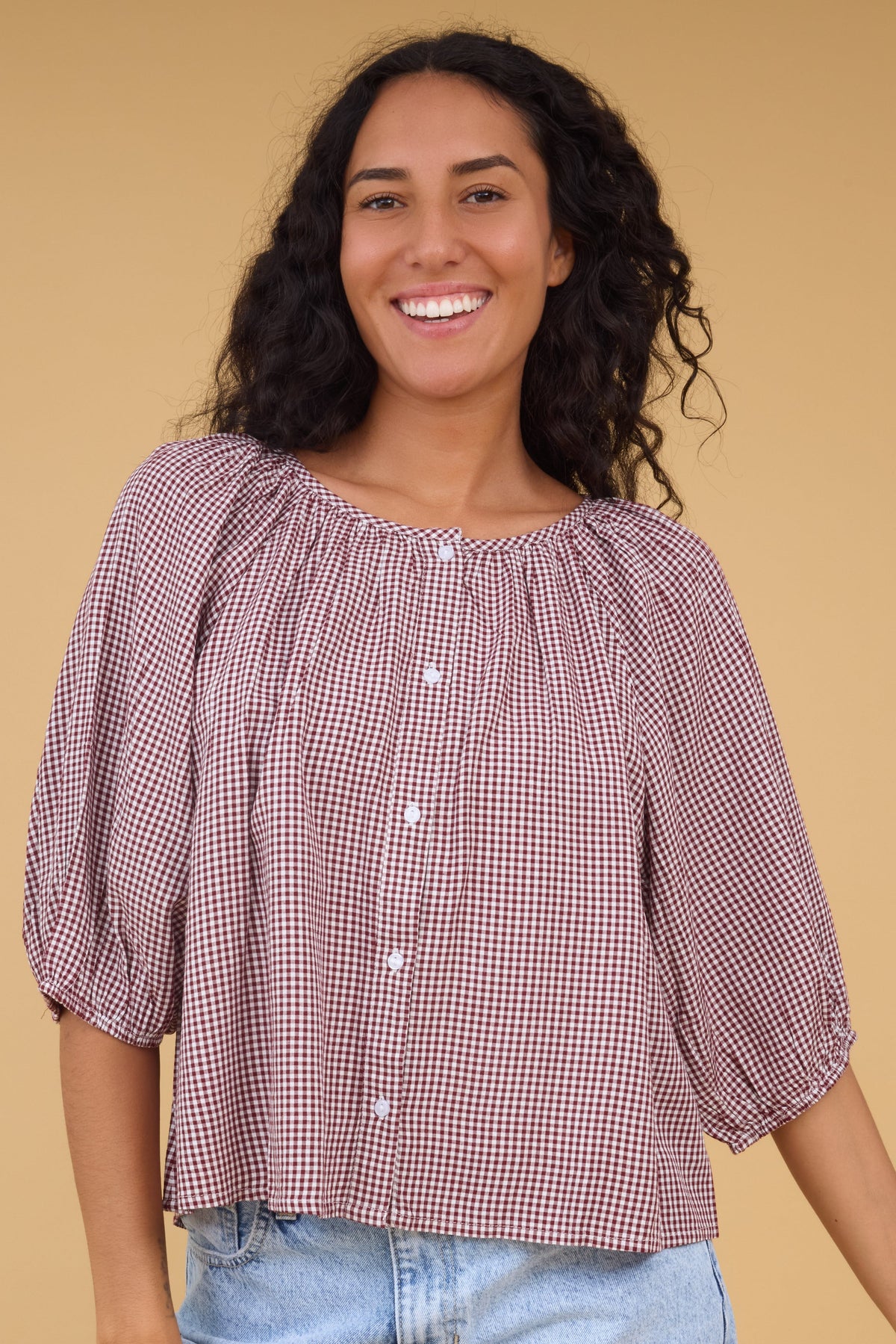 Young woman wearing a modest burgundy gingham blouse, round neckline and half length sleeves. 
